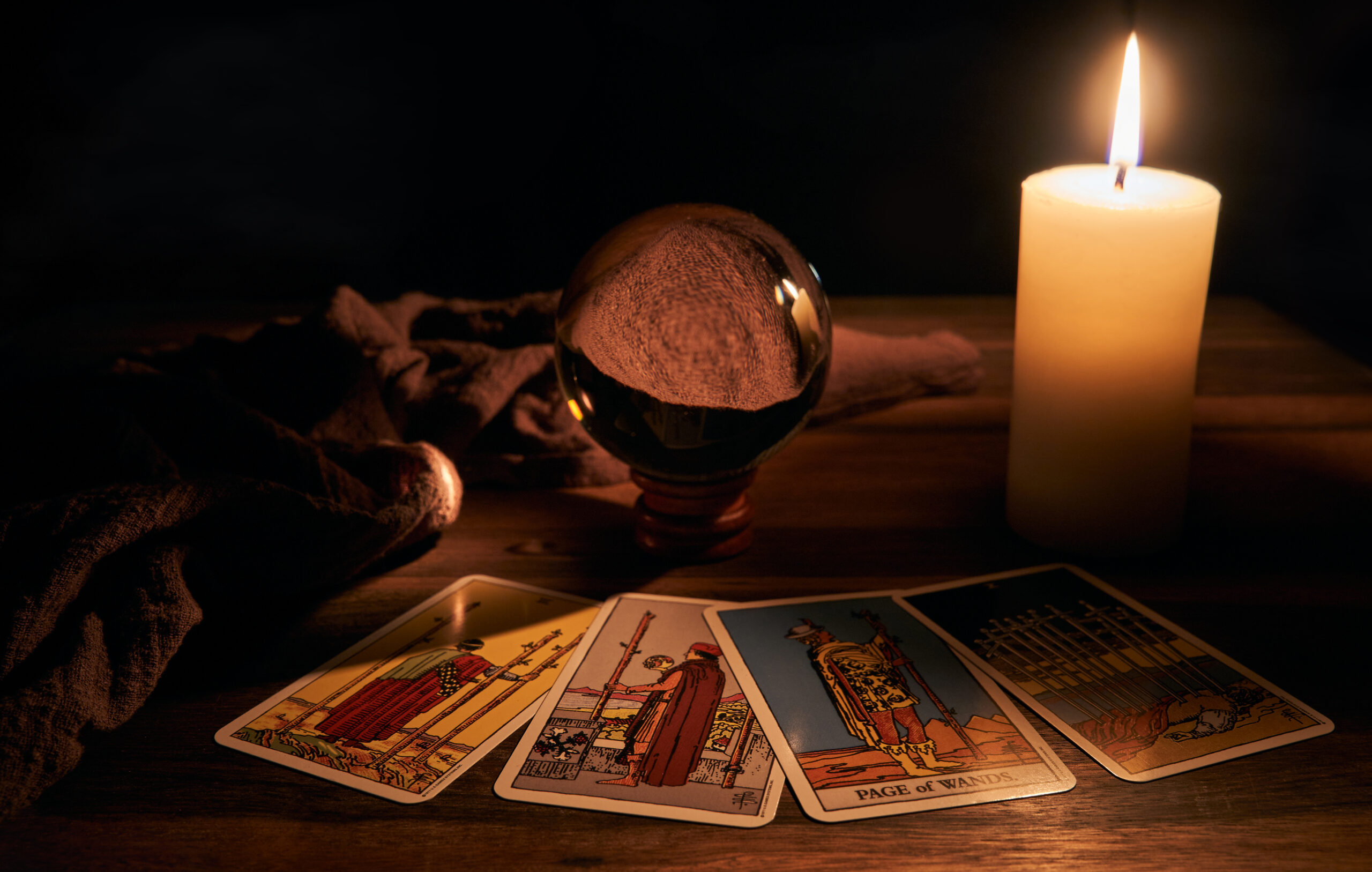 concept of fortune telling wooden table and white candle with a crystal ball and tarot cards on dark background